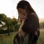 A sad pregnant woman sitting outside on the grass crying in tears covering her face.