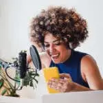 African host woman recording podcast using mobile phone at home studio - Business, podcaster technology concept
