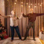An excited grandparents dancing and celebrating christmas and new year at cozy home.