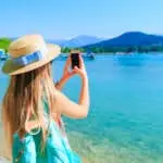 Back view of a woman with the phone in hand and do photos. beautiful lake and mountains on the background