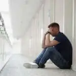 Close-up of upset man sitting on floor in hallway. Guy forgetting or losing room keys. Frustrated male sits at door. Man thinking and finding way out of situation. Bad day idea