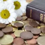 Coins, flowers, and holy bible book on rustic table. Close-up. Selective focus. Christian tithe, offering, generosity, and church contribution concept.