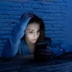 Dramatic portrait of sad scared young woman victim of online harassment and cyberbullying. looking at smart mobile phone stressed and in fear being online abused by stalker. In Dangers of internet.