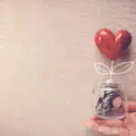 Hand holding a jar of heart tree growing on money coins, social responsibility and donation concept