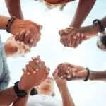 Holding hands, support and friends praying for spiritual growth, community and gratitude together with sky from below. Group of people in partnership for hope, love and human faith in connection