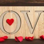 Love word written on wooden background and red rose petals