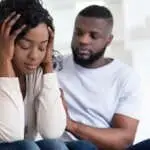 Loving african man soothing upset girlfriend, apologizing after quarrel, hugging her shoulder, empty space