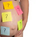 Multi-colored stickers with a question mark are glued on the belly of a pregnant girl. The concept of the uncertainty of the birth of a boy or girl, preparation for childbirth