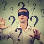 Portrait blindfolded man stretching his arms out walking through many question marks