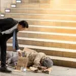 Portrait image of Businessmen's holding money gives money to a mature homeless man is Sleeping. Senior person hands begging for money