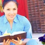 Pretty young mixed race woman in casual wear reading holy bible.