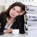 Stressed Businesswoman Working In Office With Stack Of Folders