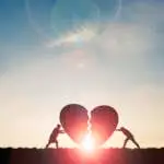 Two silhouette men pushing broken heart with sunlight and blue sky , Valentine 's day concept.