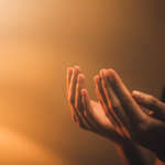 Hand praying on orange light bokeh background.