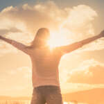 Young woman with hands up the sun light finding happiness, peace and hope