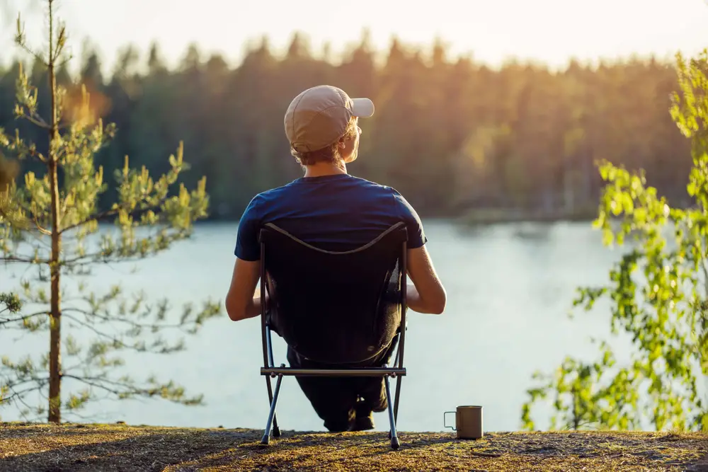 A man contemplates the evening sunset against a beautiful forest lake. The background is blurry.