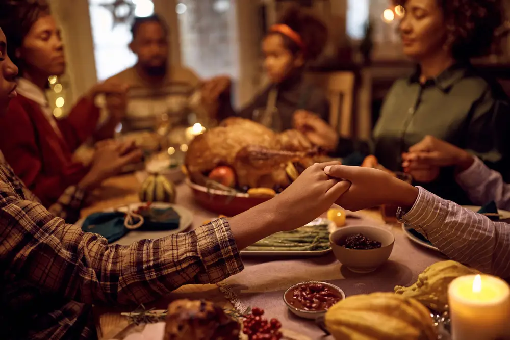 Close of kids saying grace while having Thanksgiving dinner with their family at dining table.